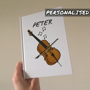 May include: A white notebook with a cello and musical notes drawn on it. The name "PETER" is written in black at the top of the notebook. The notebook is personalised.