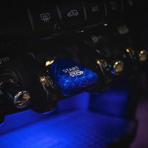 May include: A close-up of a blue car start button with the text "START ENGINE STOP" in white.