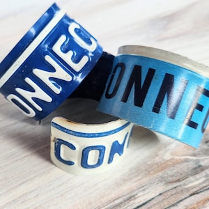 May include: Three blue and white metal rings with the word "CONNECT" printed on them. The rings are stacked on top of each other.