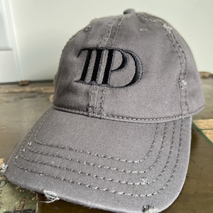 May include: A grey baseball cap with a distressed look and a black embroidered "TPD" logo.