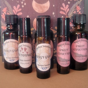May include: Five small brown glass bottles with black roll-on tops. The bottles are labeled with white text that reads "Bottled Intentions" and "Witchful Intentions". The labels also include the names of the scents: "Energy Gum", "Love Yourself", "Energy Gum", "Sweet Seduction", and "Sweet Seduction".