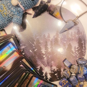 Pu&ograve; includere: Un peluche blu lavorato a uncinetto, un mazzo di carte dei tarocchi, due pendolari di cristallo e una collezione di pietre di lapislazuli blu con rune incise. Lo sfondo &egrave; un dipinto ad acquerello di una foresta illuminata dalla luna.