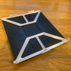 May include: A black metal plate with two silver metal frames attached to it. The frames are in the shape of a triangle and are connected by a series of metal bars.