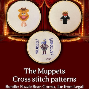 May include: Three circular wooden embroidery hoops containing cross-stitch designs on white fabric. One features a brown bear with a hat, another a character in a black suit with glasses, and the third a blue character with the text RUBES! YOKELS!