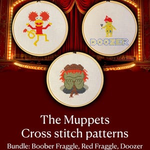 May include: Three circular wooden embroidery hoops containing cross-stitch designs. One features a red character with yellow limbs, another shows a yellow character with a red hat and the text DOOZER, and the third depicts a green character with red hair.