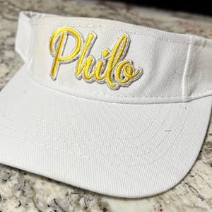 May include: White visor with a yellow embroidered "Philo" logo.