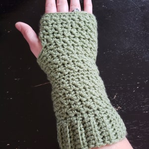 May include: Green crocheted fingerless gloves with a long cuff. The gloves are made with a simple stitch pattern.
