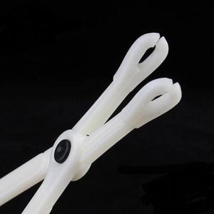 May include: White plastic tweezers with a black rubber grip. The tweezers have a rounded tip and are designed for delicate tasks.
