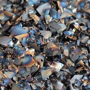 Op de afbeelding: Een close-up van een stapel metalen spaanders. De spaanders zijn een mix van zilver, blauw en bruin. De spaanders zijn scherp en hebben verschillende vormen en maten.