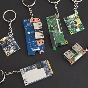 May include: Six different circuit boards with various components, including USB ports, are attached to keychains. The circuit boards are green, blue, and black. The keychains are silver.