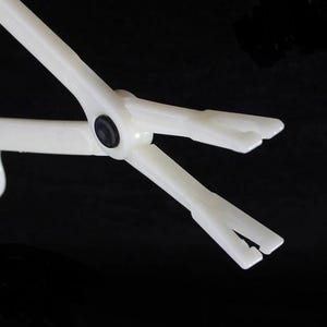 May include: White plastic tweezers with a black hinge. The tweezers have two prongs at the end.