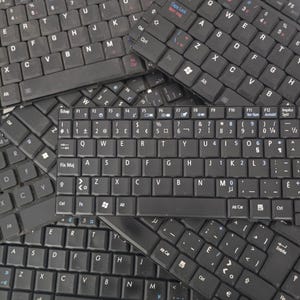 Puede incluir: Primer plano de varios teclados de ordenador negros con diferentes teclas y etiquetas. Los teclados están dispuestos de forma aleatoria, creando un fondo texturizado.