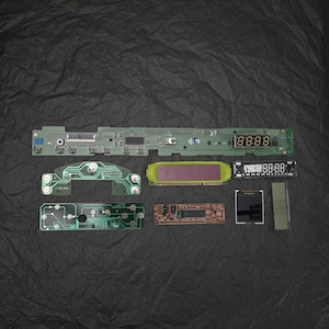 Peut inclure: Ensemble de circuits imprimés électroniques et d'écrans numériques, dont une carte de circuit imprimé verte avec le numéro "37" et un affichage numérique indiquant "88:88". D'autres composants incluent un écran jaune et vert et un petit écran noir.