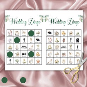 May include: Two sheets of "Wedding Bingo" game cards with green accents and floral designs. Each card features a grid of wedding-themed images and words. A pair of gold scissors rests on the right side of the cards.
