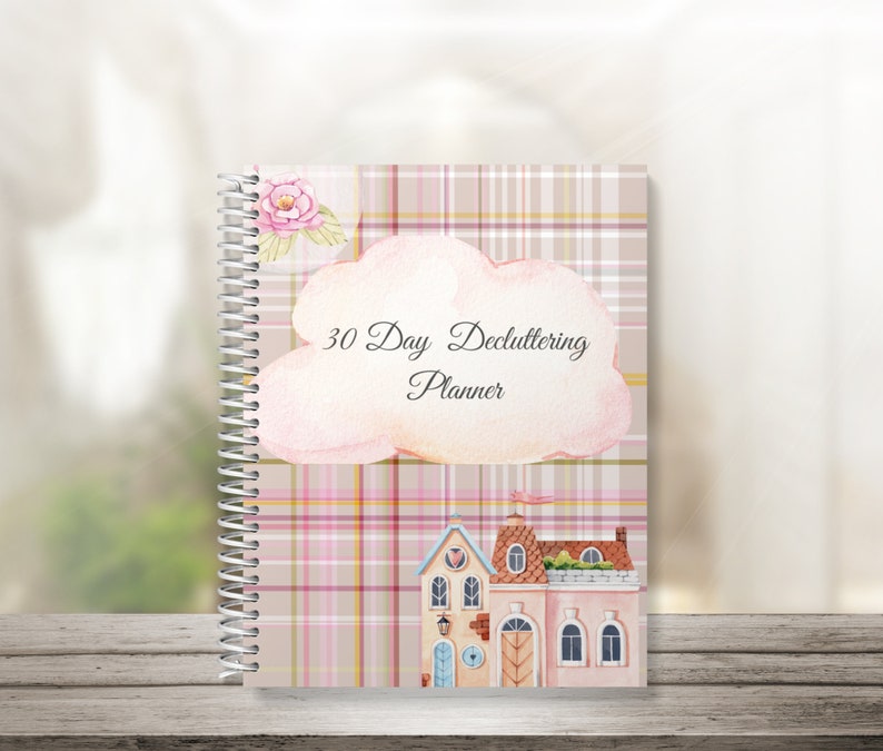 May include: A pink and beige plaid planner with a watercolor cloud and the text "30 Day Decluttering Planner". The planner also features a watercolor illustration of a pink and yellow house with a pink roof.