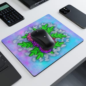 Puede incluir: Un ratón de ordenador inalámbrico negro descansa sobre una alfombrilla rectangular. La alfombrilla presenta un diseño floral con rosas rosas y moradas, hojas verdes y un fondo azul y morado. Otros aparatos electrónicos son visibles.