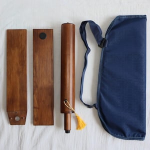 May include: A set of wooden folding chairs with a blue canvas carrying case. The chairs have a dark brown finish and a small black knob on each leg. The case has a strap and a tassel.