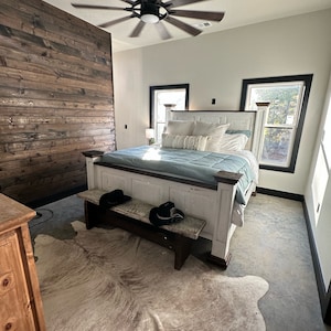 May include: A white bedroom with a large bed, a cowhide rug, and a wooden bench. The bed has a white headboard and a blue blanket. The room has a ceiling fan and two windows with black frames.