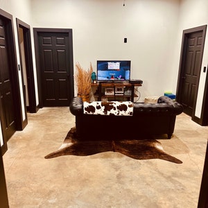 May include: A living room with a brown leather couch, a cowhide rug, and a flat screen TV on a wooden shelf. There are three black doors in the room, and a ceiling fan with wooden blades.