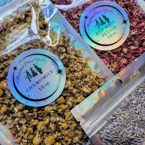 May include: Three resealable bags of dried herbs, each with a holographic label. The first bag contains chamomile flowers, the second bag contains red rose petals, and the third bag contains lavender flowers. Each bag is labeled with the name of the herb and the weight, 1/2 oz.