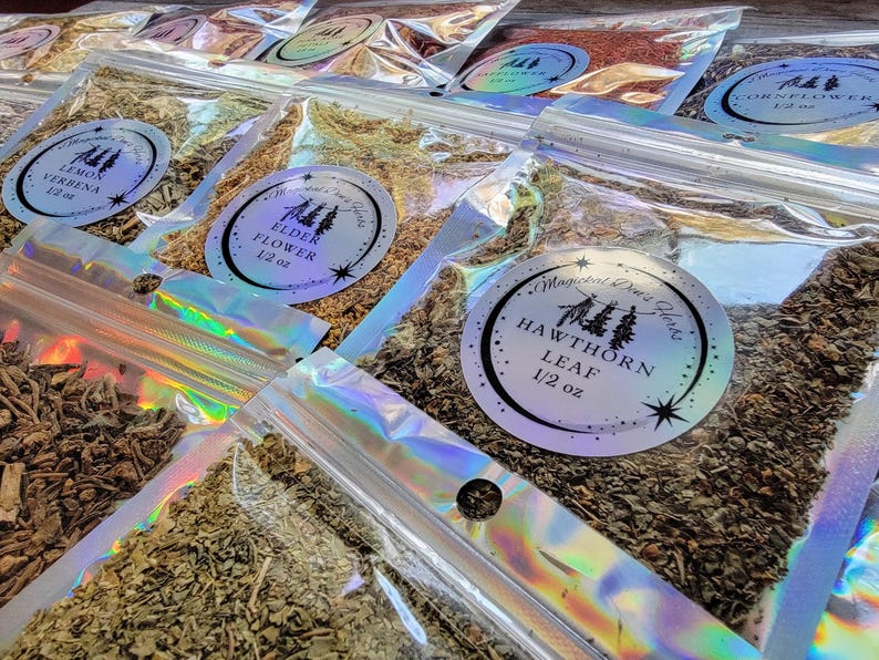 May include: A variety of dried herbs and flowers packaged in clear plastic bags with labels. The labels are white with black text and feature a small tree design. The herbs and flowers include elderflower, lemon verbena, hawthorn leaf, and cornflower. Each bag contains 1/2 ounce of herbs or flowers.