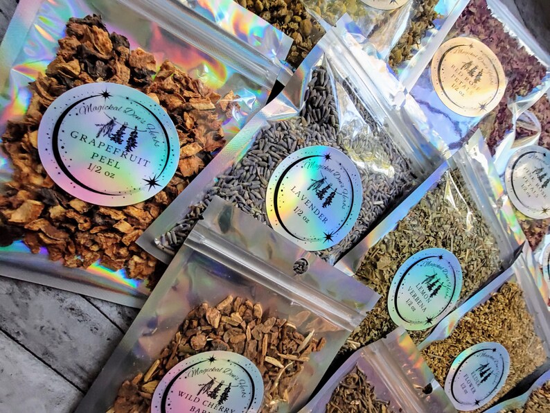 May include: A collection of small, clear plastic bags filled with dried herbs and flowers. Each bag has a label with the name of the herb and the weight. The herbs include grapefruit peel, lavender, lemon verbena, wild cherry bark, and a floral blend.