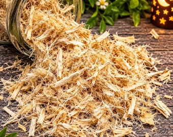 May include: A clear glass jar tipped on its side, spilling out a pile of light tan, fibrous, shredded wood material. The texture is stringy and dry, consisting of thin, splintered pieces of natural wood scattered across the surface.