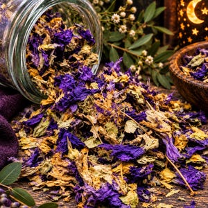 May include: A clear glass jar tipped on its side, spilling a mixture of dried purple flower petals and light tan dried leaves. The botanical blend is scattered across a dark wooden surface, with a small wooden bowl visible to the right side.