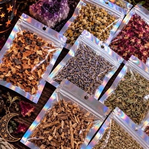 Op de afbeelding: Een verzameling kleine, doorzichtige, holografische hersluitbare zakjes gevuld met diverse gedroogde kruiden, bloemen en botanische ingredi&euml;nten, waaronder sinaasappelschil, lavendel, kamille en rozenblaadjes op een donkere houten ondergrond.