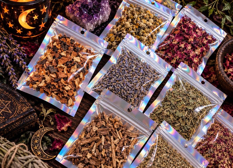 Op de afbeelding: Een verzameling kleine, doorzichtige, holografische hersluitbare zakjes gevuld met diverse gedroogde kruiden, bloemen en botanische ingredi&euml;nten, waaronder sinaasappelschil, lavendel, kamille en rozenblaadjes op een donkere houten ondergrond.