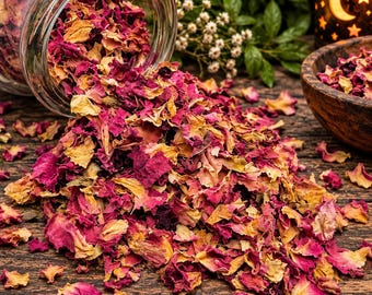 May include: A clear glass jar tipped on its side, spilling a mixture of dried rose petals in shades of deep magenta, vibrant pink, and muted yellow. The scattered petals form a pile on a dark, textured wooden surface, with a small wooden bowl nearby.