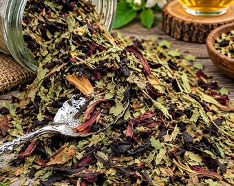May include: A clear glass jar tipped over, spilling a loose-leaf herbal tea blend of dried dark red hibiscus petals and green leaves onto a wooden surface. A silver ornate spoon rests in the tea pile, with a glass of amber tea nearby.