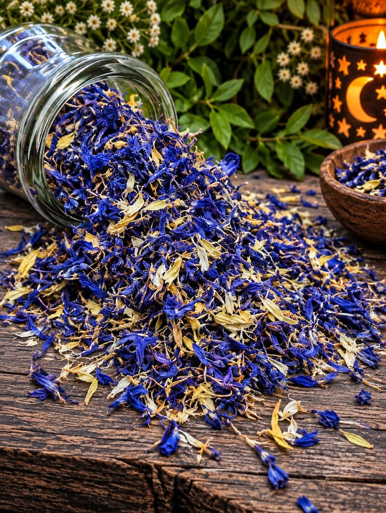 Op de afbeelding: Een glazen pot die op zijn kant ligt en een mengsel van gedroogde blauwe korenbloemblaadjes en lichtgele botanische stukjes morst op een donkerhouten oppervlak. De gedroogde bloemenmix ligt verspreid, met een kleine houten kom ernaast.