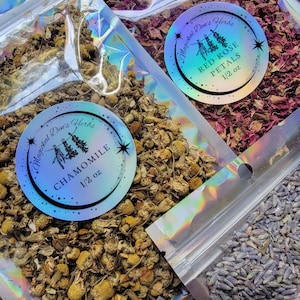 May include: Three resealable bags of dried herbs, each with a holographic label. The labels feature a whimsical tree design and the names of the herbs: Chamomile, Red Rose Petals, and Lavender. Each bag contains 1/2 ounce of herbs.