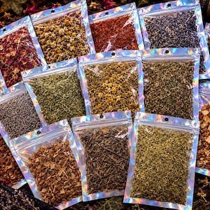 May include: A collection of small, clear holographic zip-lock pouches filled with various dried herbs, flowers, and botanical ingredients, including red rose petals, yellow chamomile, purple lavender, green leaves, and brown bark pieces.