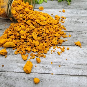 May include: A glass jar with a yellow, granular spice spilling out onto a gray wooden surface. The spice is turmeric.