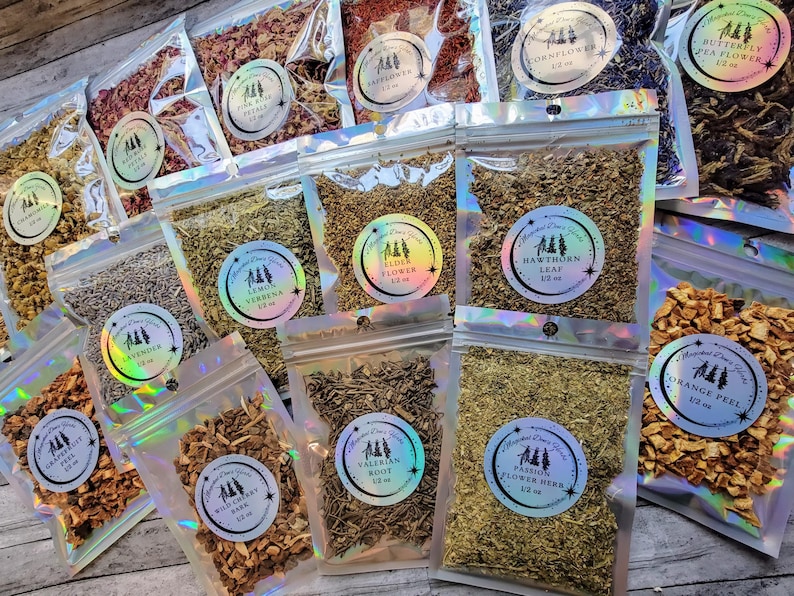 May include: Assortment of 12 small, clear, resealable bags filled with various dried herbs and flowers. Each bag has a label with the name of the herb or flower and the weight in ounces. The herbs and flowers are a variety of colors, including brown, green, white, and purple.