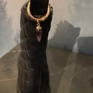 Könnte beinhalten: Schwarze gesteppte Stiefeletten mit einem goldenen Ring und einem violetten Kristall-Anhänger.