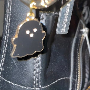 Könnte beinhalten: Schwarze Lederstiefel mit gelben Nähten und einem goldenen Reißverschluss. Der Reißverschluss hat einen schwarzen Geisteranhänger mit weißen Augen.
