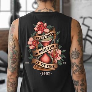 May include: Black tank top with a floral and hourglass design. The design includes the text "EVERYTHING IS BEAUTIFUL IN ITS TIME" on a banner, with the brand name "FLCO" below. The tank top is sleeveless.