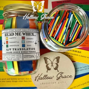 May include: A glass jar filled with colorful paper strips, each with a Bible verse written on it. The jar has a label that reads "Read Me When..." with a list of emotions like "Happy", "Thankful", "Anxious", "Angry", "Lonely", and "Sad". The jar is sitting on a table with other Bible verses and a wooden coaster with a butterfly design and the words "Hallow Grace Christian Gifts".