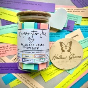 May include: A glass jar filled with colourful paper slips, labelled "Confirmation Jar". The jar has a wooden lid with the name "Bella Ann Smith" and the date "May 4, 2024". The jar is surrounded by colourful paper slips with bible verses.