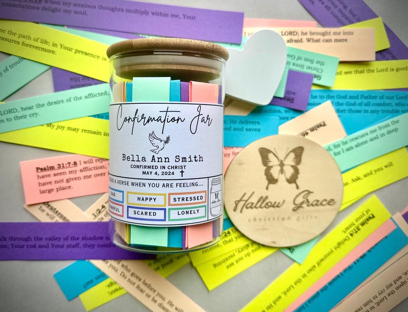 May include: A glass jar filled with colourful paper slips, labelled "Confirmation Jar". The jar has a wooden lid with the name "Bella Ann Smith" and the date "May 4, 2024". The jar is surrounded by colourful paper slips with bible verses.