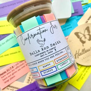 May include: A glass jar filled with colorful paper slips, labeled "Confirmation Jar". The jar has a white label with the name "Bella Ann Smith" and the date "May 4, 2024". The label also includes the text "CONFIRMED IN CHRIST" and a small cross symbol. Below the name, there are five colored boxes with the words "SAD", "HAPPY", "SCARED", "STRESSED", and "LONELY".