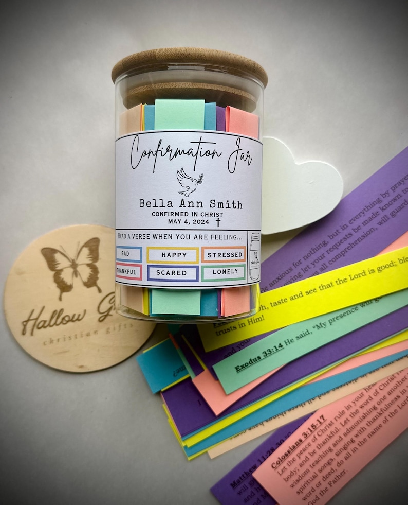 May include: A glass jar with a wooden lid filled with colourful paper strips. The jar has a label that reads "Confirmation Jar" and includes the name "Bella Ann Smith" along with the date "May 4, 2024". The label also includes the text "CONFIRMED IN CHRIST" and "READ A VERSE WHEN YOU ARE FEELING..." with a list of emotions: "SAD", "THANKFUL", "HAPPY", "STRESSED", "SCARED", and "LONELY".