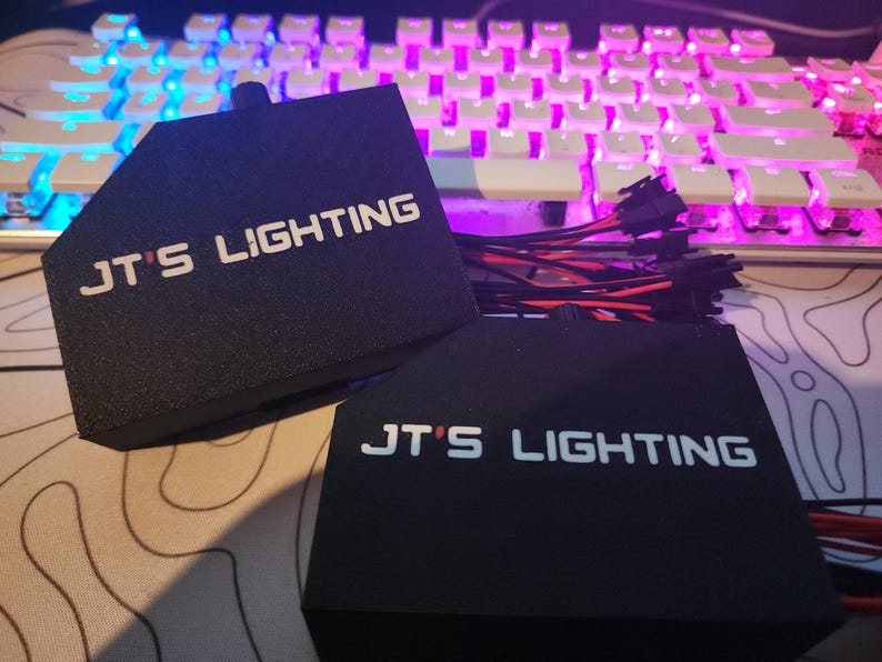 Puede incluir: Dos cajas rectangulares negras con el texto "JT's Lighting" en letras blancas. Las cajas est&aacute;n conectadas por un haz de cables con conectores.