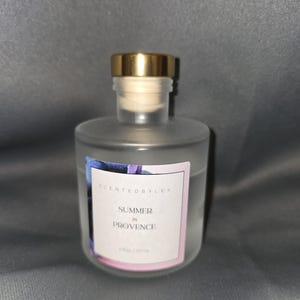 May include: A clear glass bottle with a gold lid and a white label that reads "Scented by Ley Summer in Provence 250g/8.8oz".
