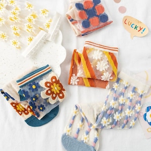 May include: Five pairs of sheer socks with floral embroidery. The socks are in various colors and patterns, including orange, yellow, blue, and white.