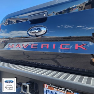 May include: Close-up of a black Ford Maverick truck tailgate. The word "MAVERICK" is in bright red lettering. The Ford logo is visible above the lettering. The image also includes the Ford Official Licensed Product logo.