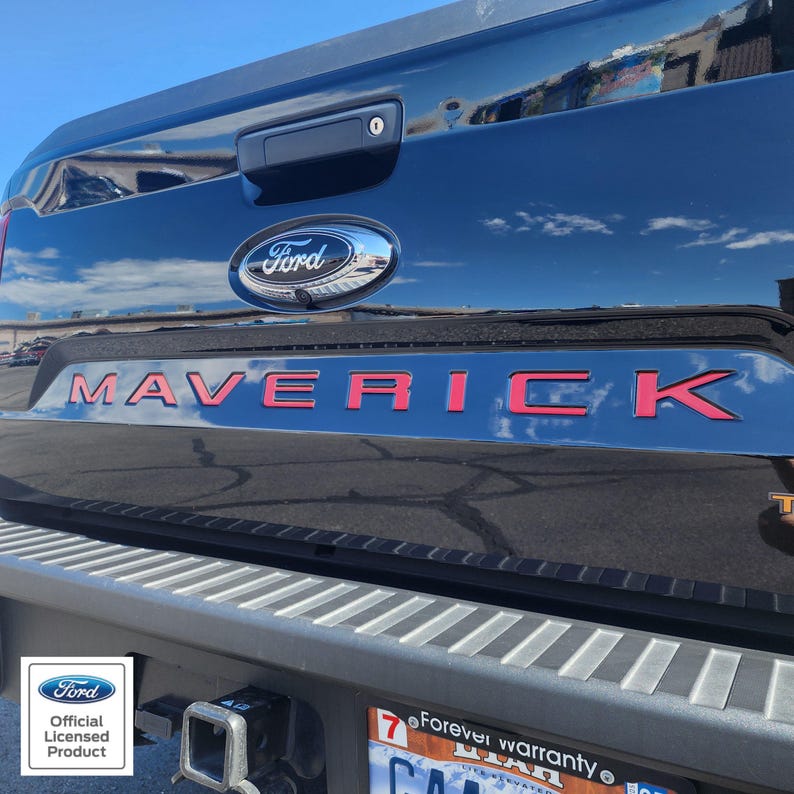 May include: Close-up of a black Ford Maverick truck tailgate. The word "MAVERICK" is in bright red lettering. The Ford logo is visible above the lettering. The image also includes the Ford Official Licensed Product logo.